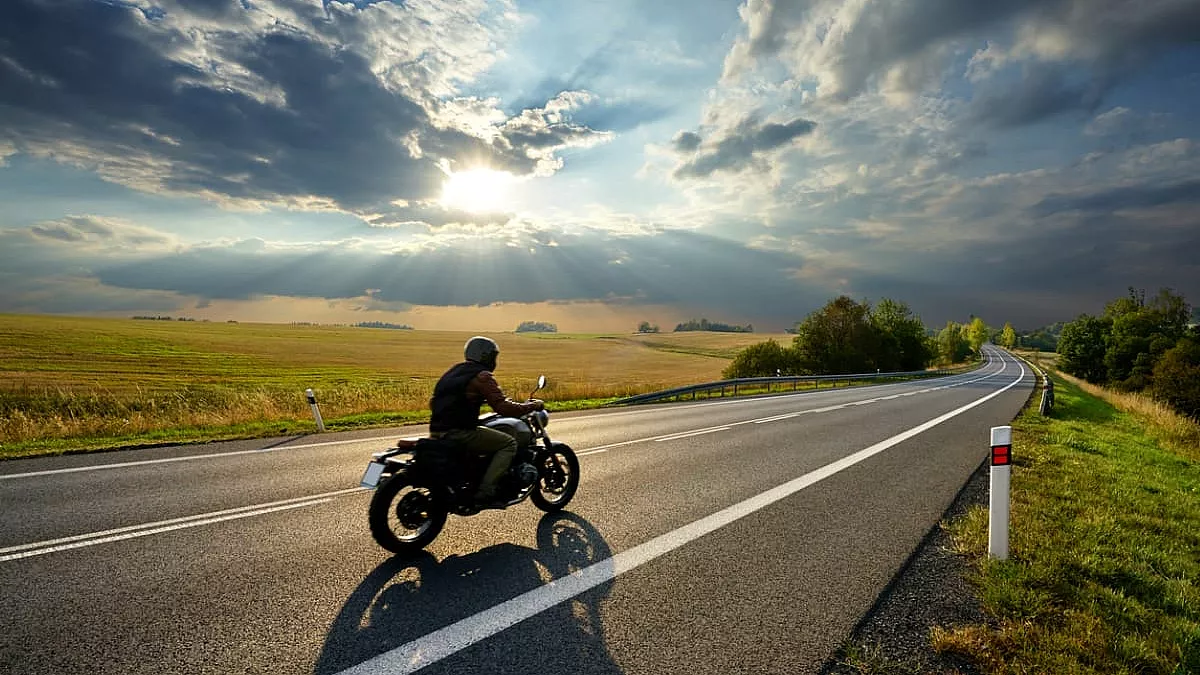 Motociclista in sella alla sua moto mentre viaggia per stade di campagna. iStock/Milos-Muller