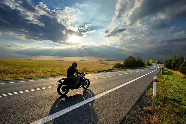 Motociclista in sella alla sua moto mentre viaggia per stade di campagna. iStock/Milos-Muller